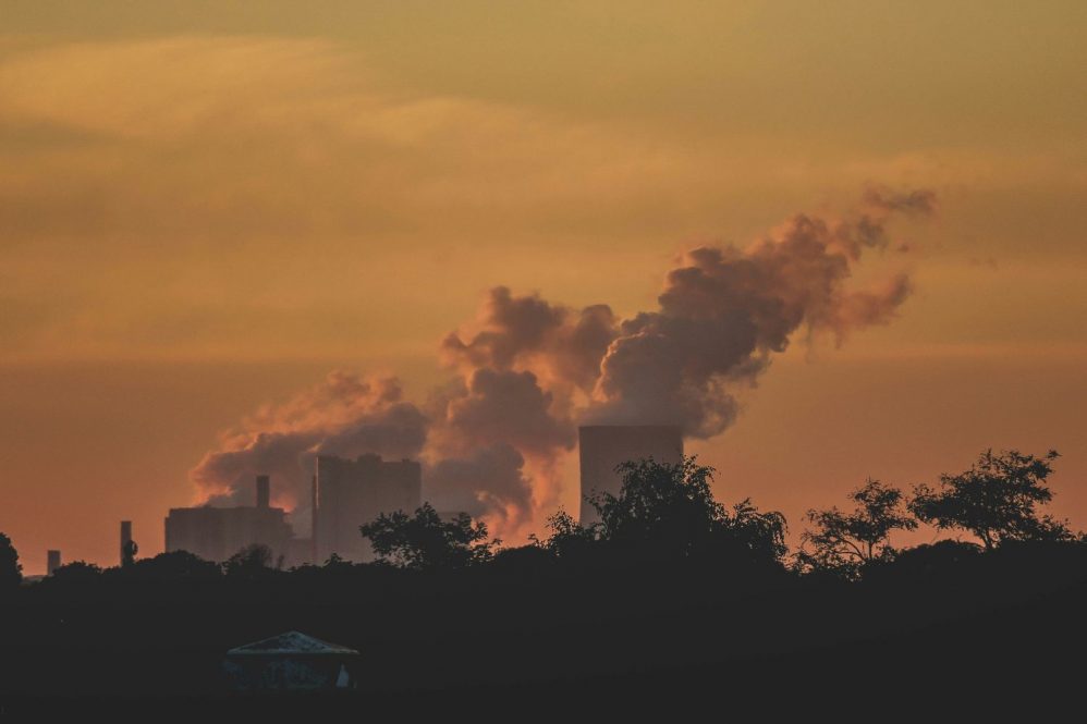 Powerplant with smoke over trees at sunset