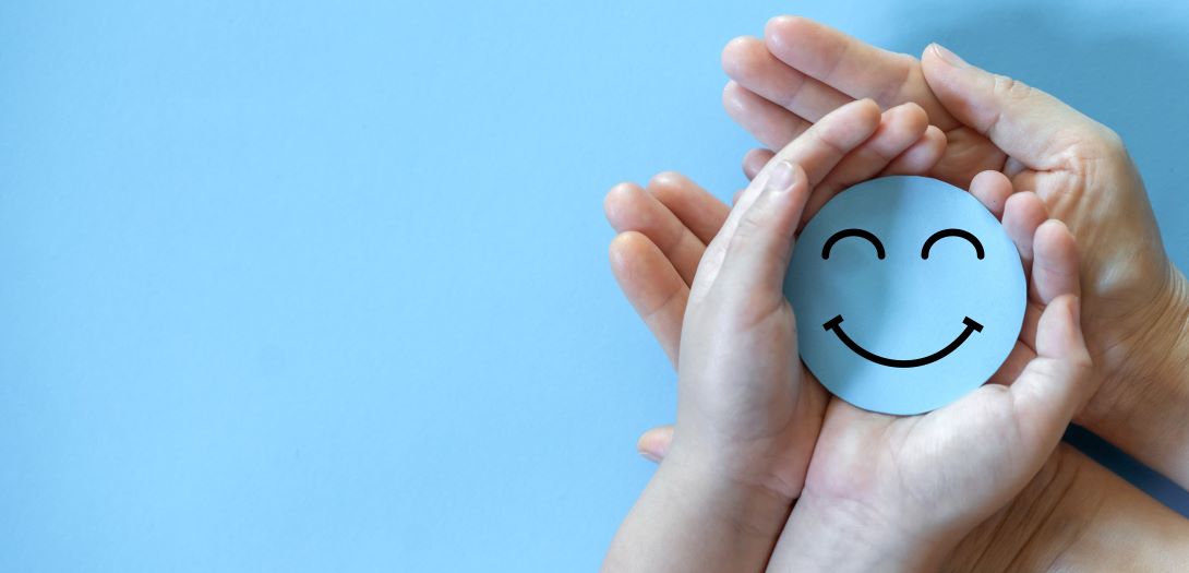 Two pairs of hands hold a blue smiley face against a blue background